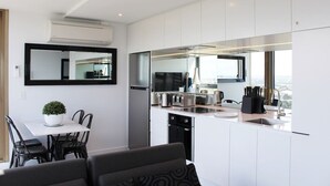 A modern kitchen with a dining area, featuring a large island, stainless steel appliances, and a view of the city. - Luxurious Flemington with Stunning Racecourse View (Kensington)