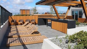 A rooftop terrace with wooden loungers, a wooden pergola, and a black outdoor kitchen. - Luxurious Flemington with Stunning Racecourse View (Kensington)
