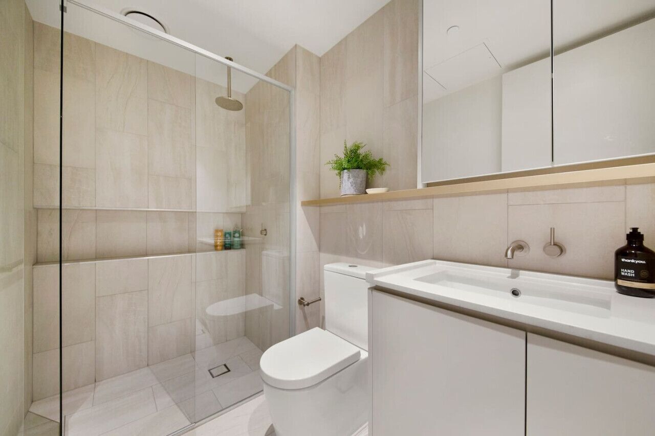 A modern bathroom with a glass shower enclosure, a toilet, a sink, and a mirror above the sink.