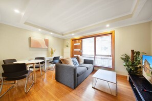 A modern living room with a grey sofa, black chairs, a small table, and a TV on a stand. - Fly Around Town in Pocket Rocket (Albion)