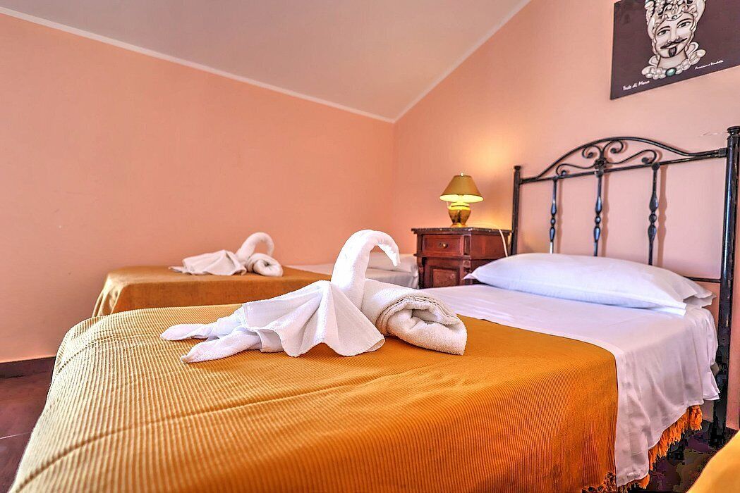 A hotel room with two beds, each with a white towel and a decorative swan towel. There is a nightstand with a lamp and a framed picture on the wall.