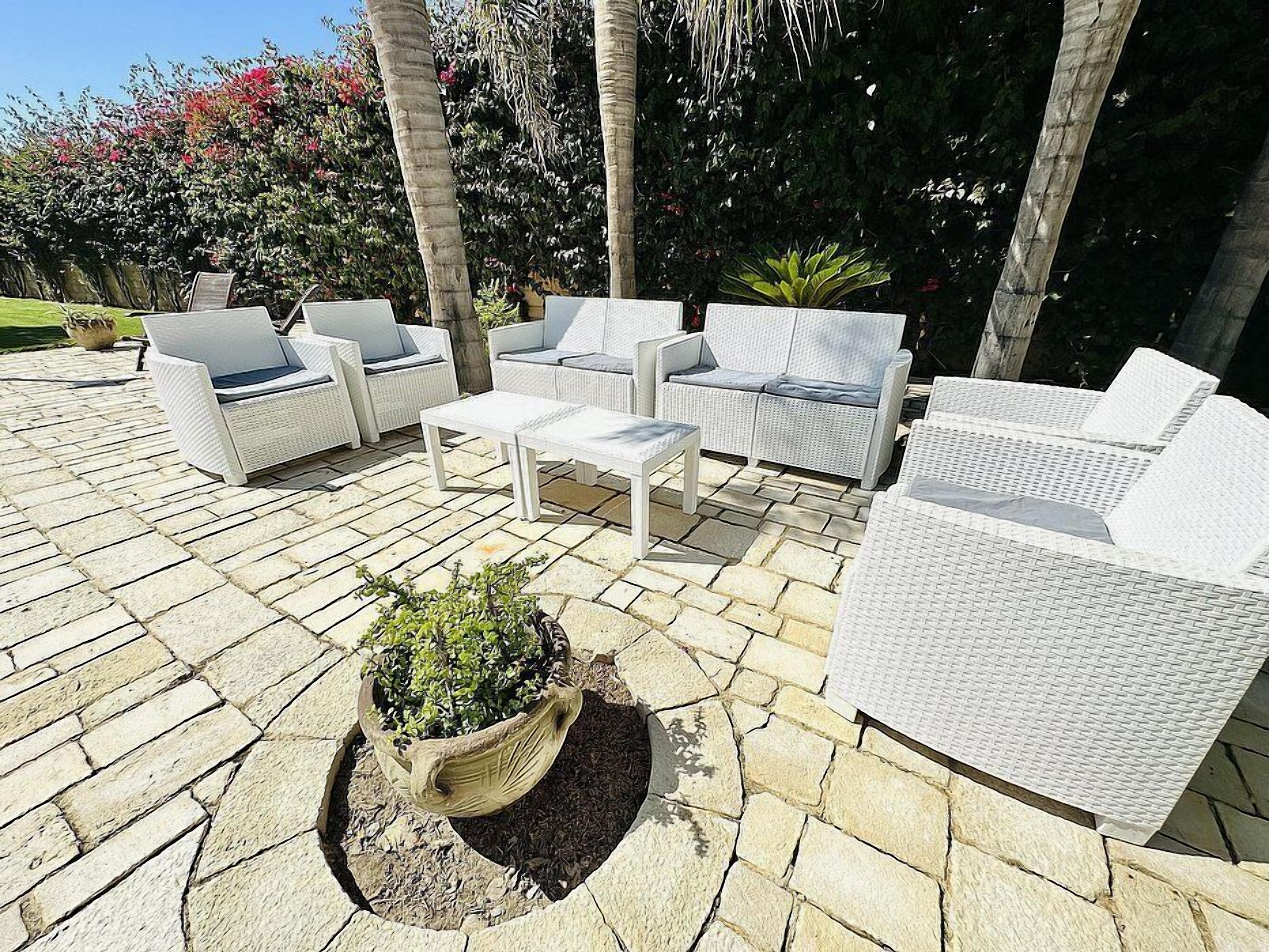 Un espace extérieur aménagé en terrasse, avec des meubles en osier blanc, notamment des canapés et une table basse, disposés sur un sol carrelé en pierre.