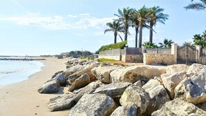 Une plage avec de gros rochers au premier plan, une clôture en bois et des palmiers.