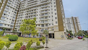 Un immeuble résidentiel à plusieurs étages, doté de balcons, d’une entrée principale et d’un jardin bien entretenu.