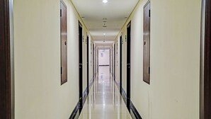 Un long couloir étroit, typique d’un hôtel, avec des portes des deux côtés, un sol carrelé et un plafond doté d’un éclairage encastré.