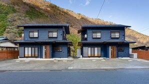 Two identical blue houses with a garage, a driveway, and a hillside in the background. - SMART VILLA Hakone Sukumogawa Riverside (Hakone)