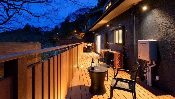 A wooden deck with a table and chairs, a wine bottle, and glasses. - SMART VILLA Hakone Sukumogawa Riverside (Hakone)