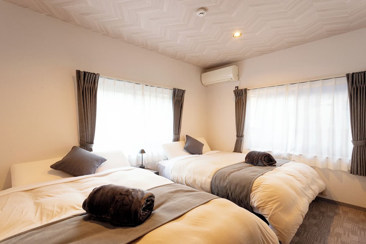 A hotel room with two beds, a ceiling light, and an air conditioning unit.