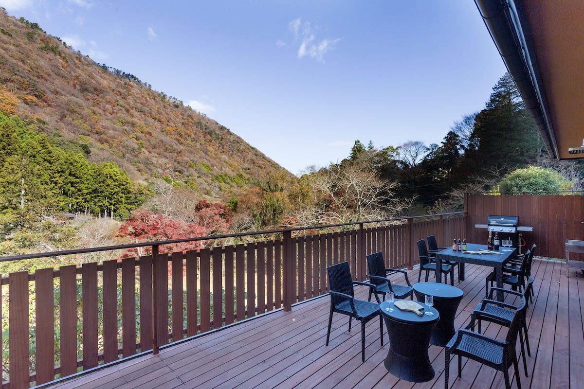 A deck with outdoor seating, a barbecue grill, and a view of a hillside.