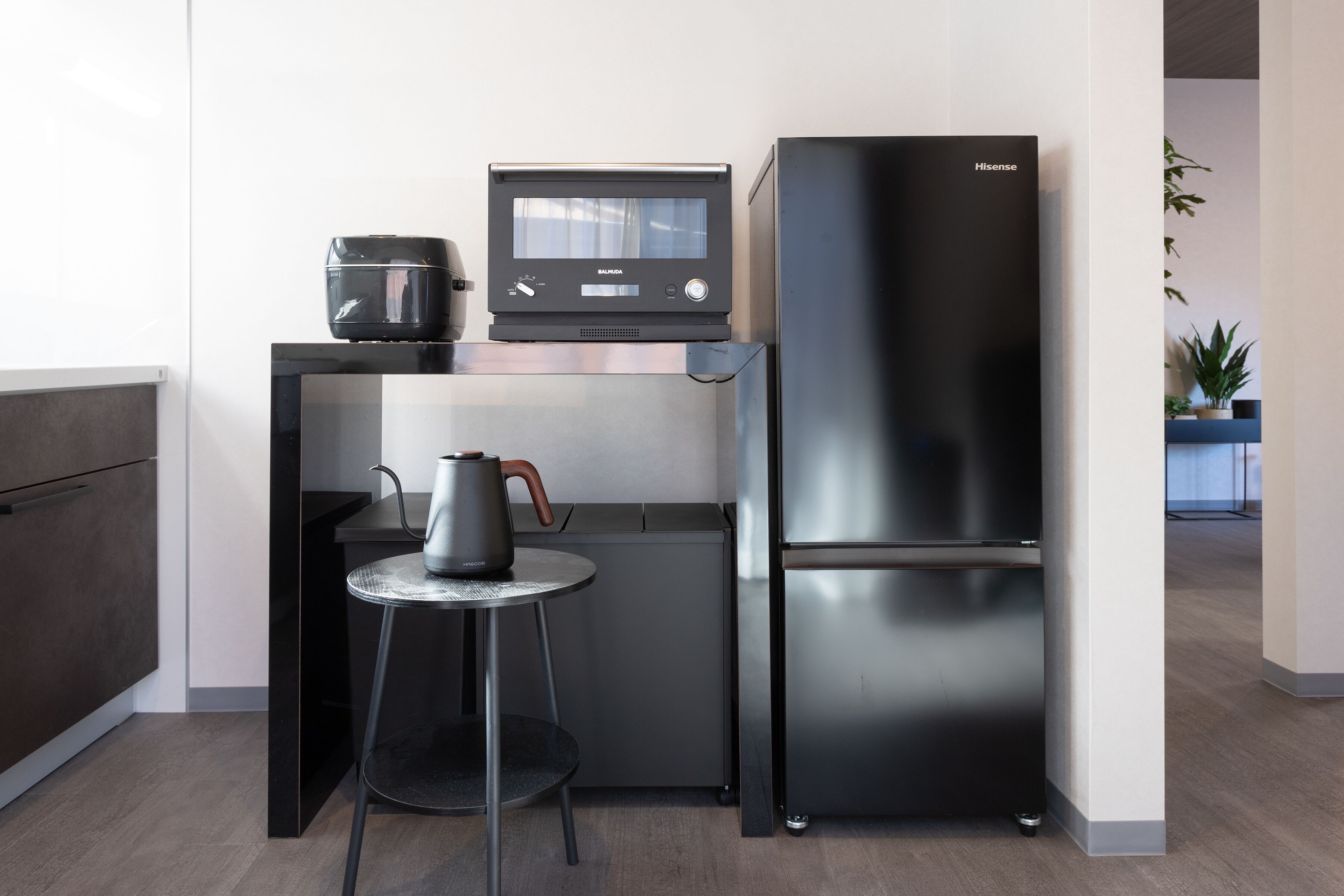 Una cocina compacta con un refrigerador negro moderno, una cafetera y una pequeña mesa con una silla.