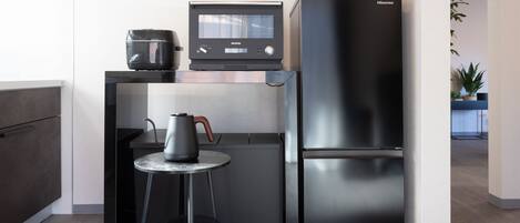 Una cocina compacta con un refrigerador negro moderno, una cafetera y una pequeña mesa con una silla.