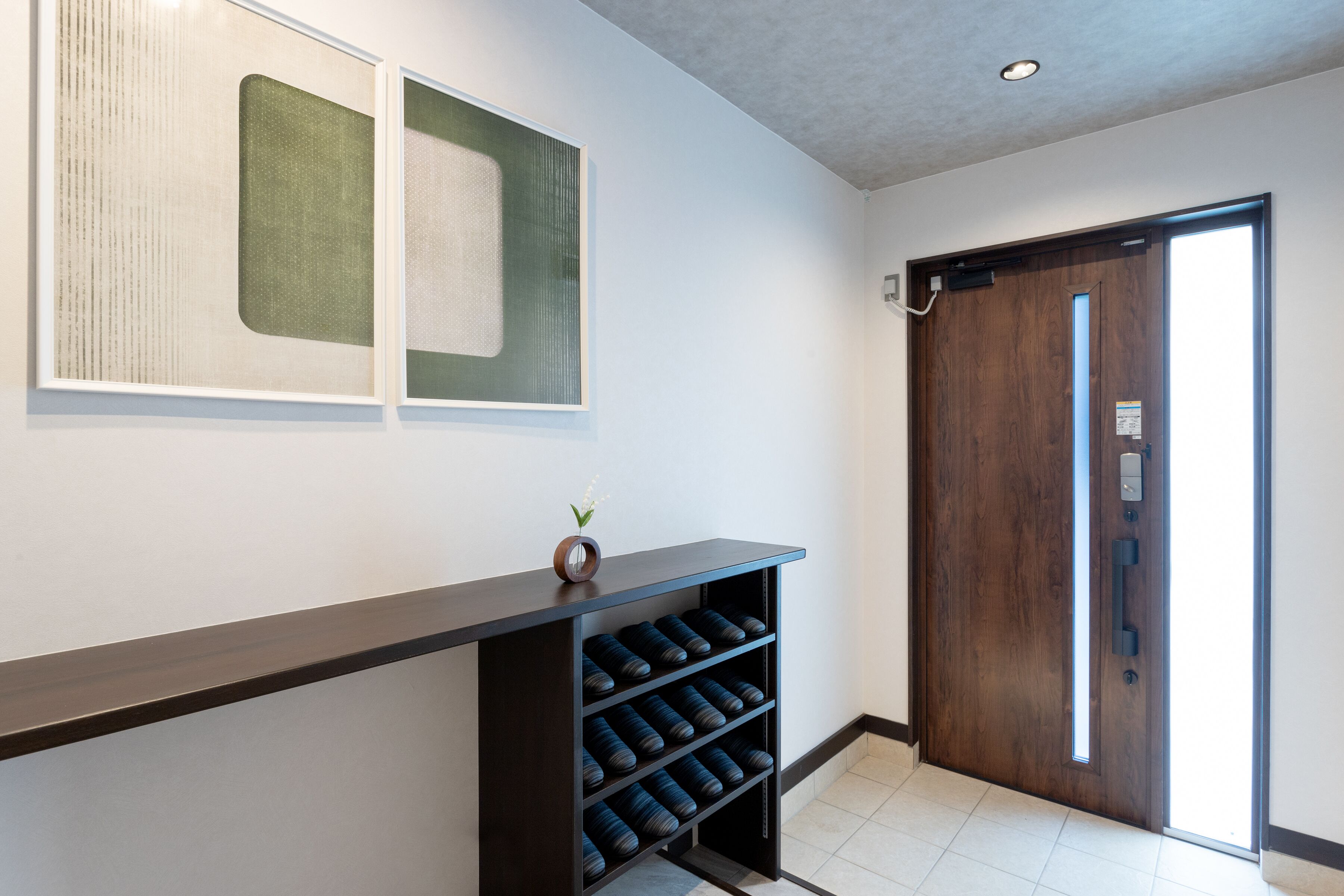 A reception area with a dark wooden reception desk, a wall-mounted vase with a plant, and a wooden door with a handle.
