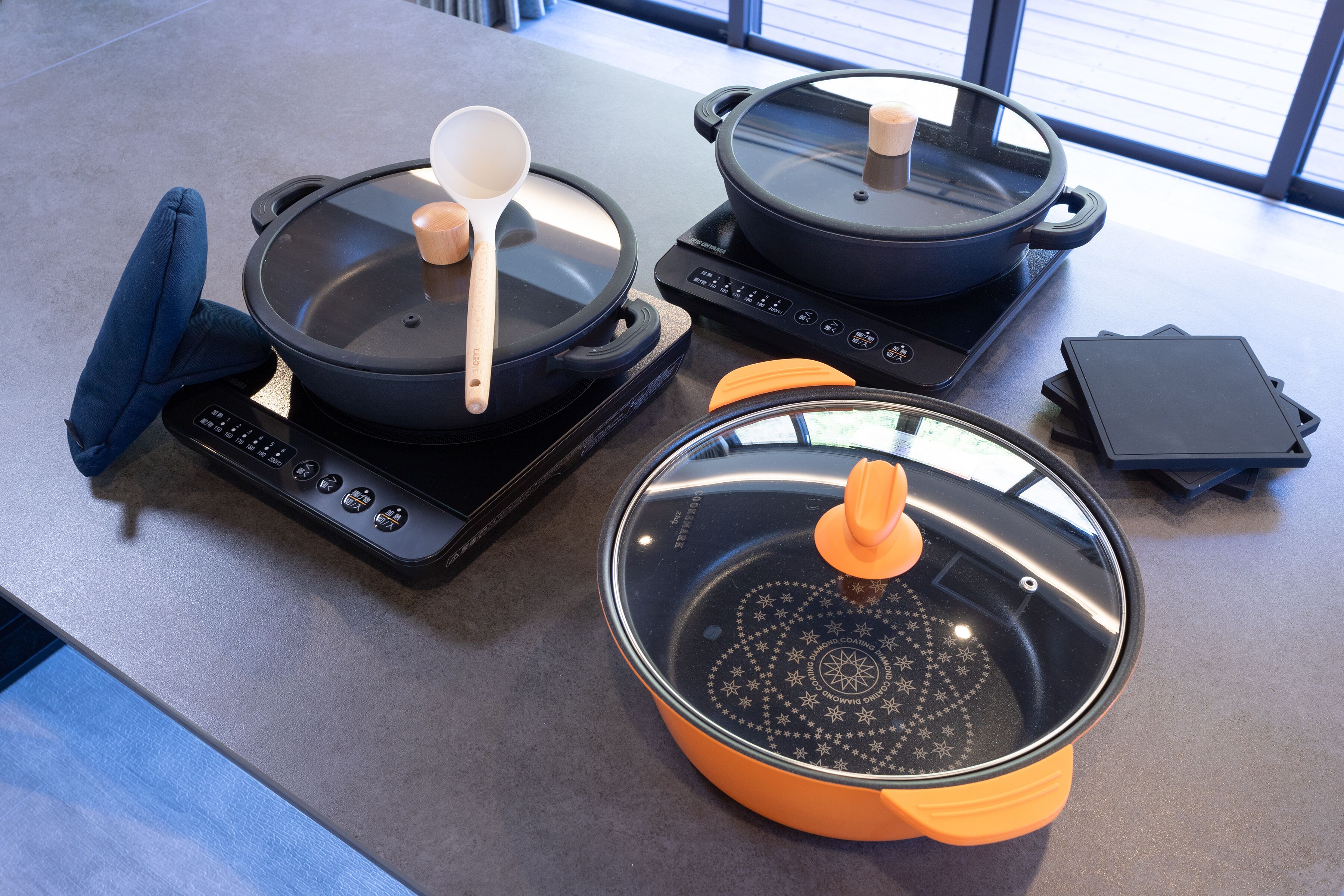 A kitchen with two induction cooktops, a blue oven mitt, and a black appliance control panel.
