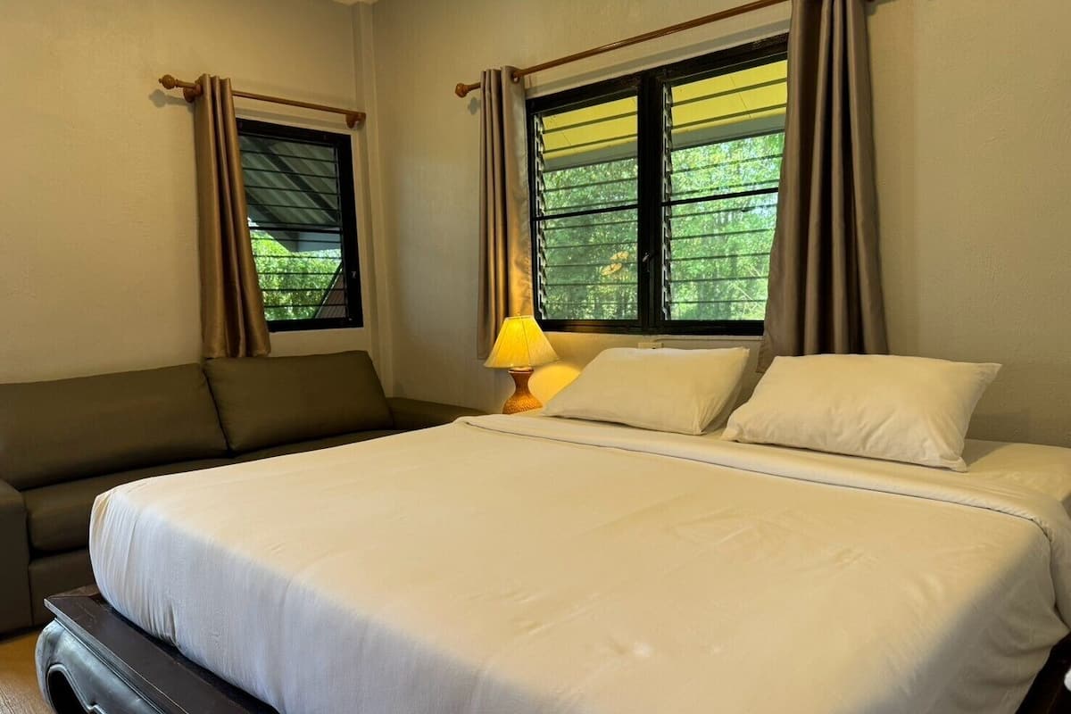 Una habitación de hotel con una cama grande, un sofá y dos ventanas con cortinas.