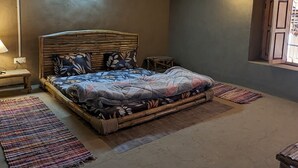 Une chambre à coucher avec un lit en bois, une table de chevet, une petite table et une fenêtre avec des barreaux.