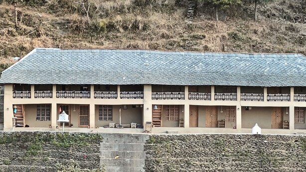 Un bâtiment à deux étages, doté d’un toit en tuiles, de plusieurs balcons et d’un mur en pierre à l’avant.