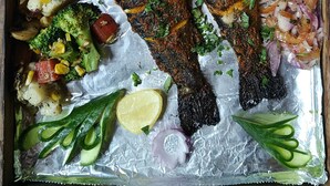Un plateau avec du poisson grillé, des légumes et une sauce verte.
