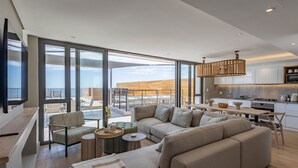 A modern living room with a large sofa, a dining area, and a kitchen. - Plett Quarter Apartments (Plettenberg Bay)
