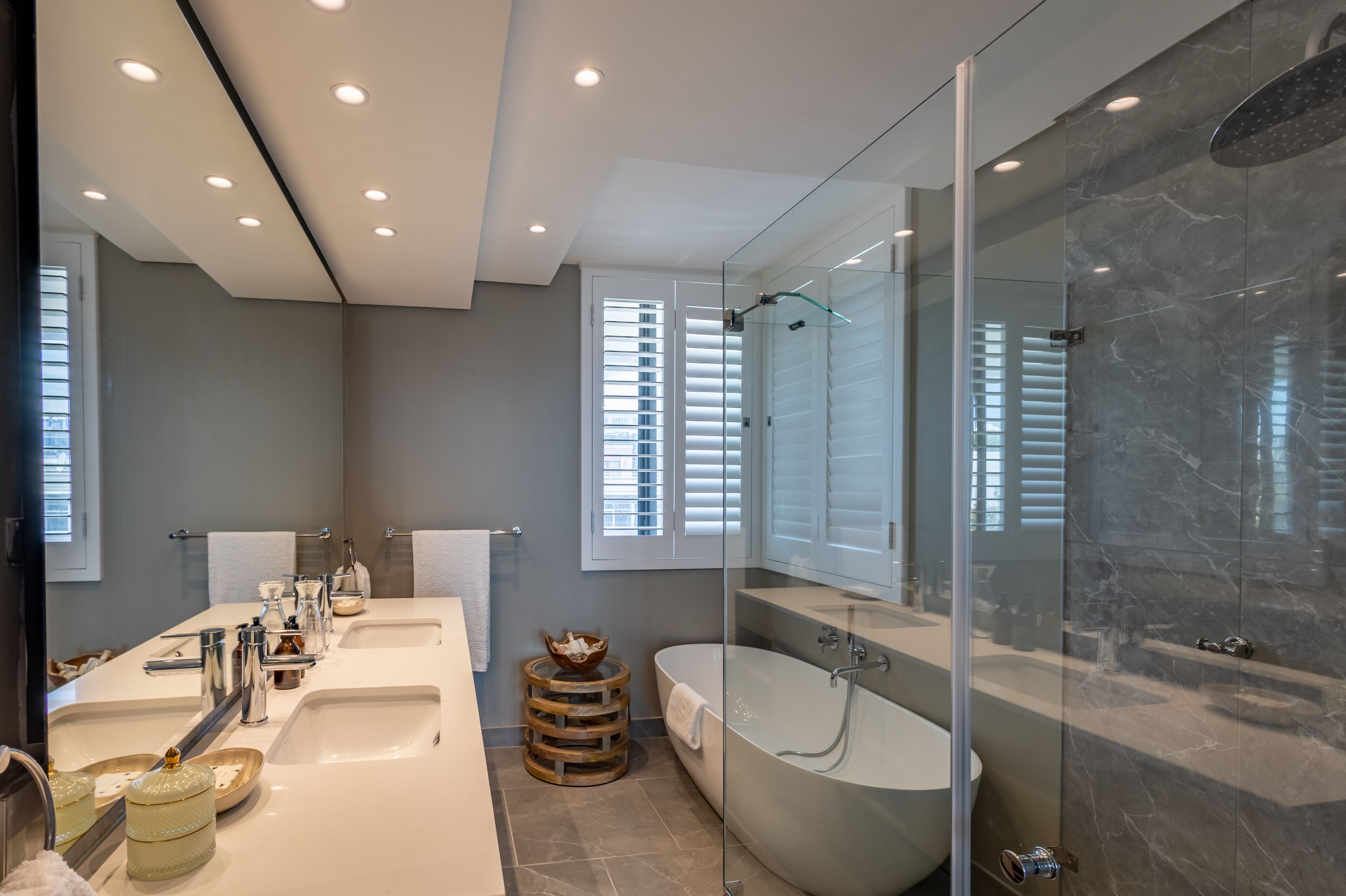 Un baño moderno con una bañera grande, una ducha con mampara de vidrio y un lavamanos con varios lavabos.