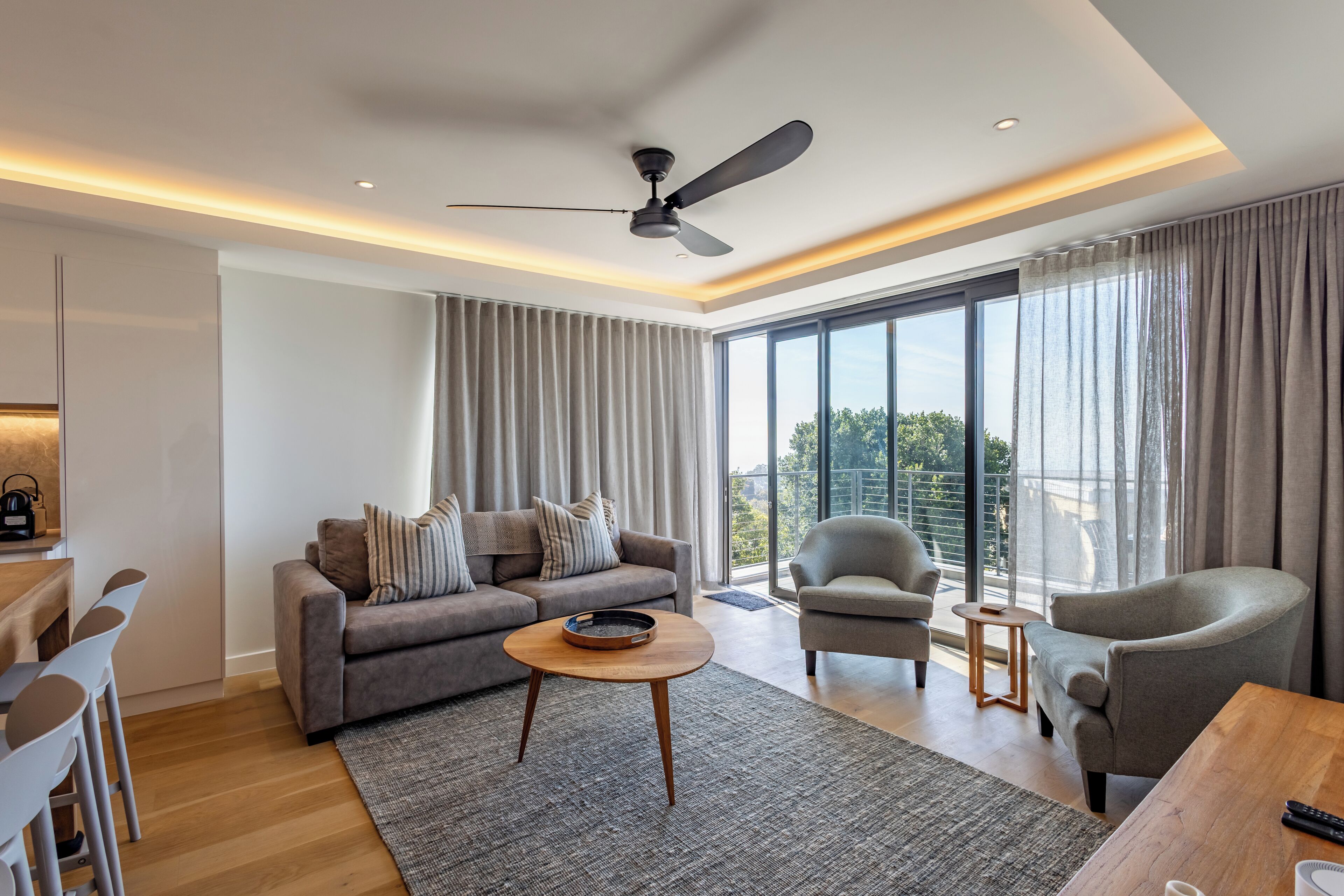 A modern living room with a sofa, armchairs, a coffee table, and a ceiling fan.