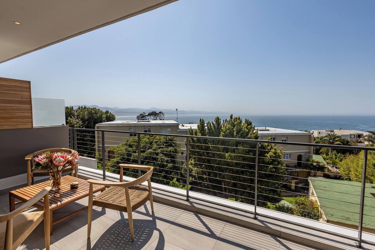 A balcony with a view of the sea, a table with chairs, and a vase of flowers.