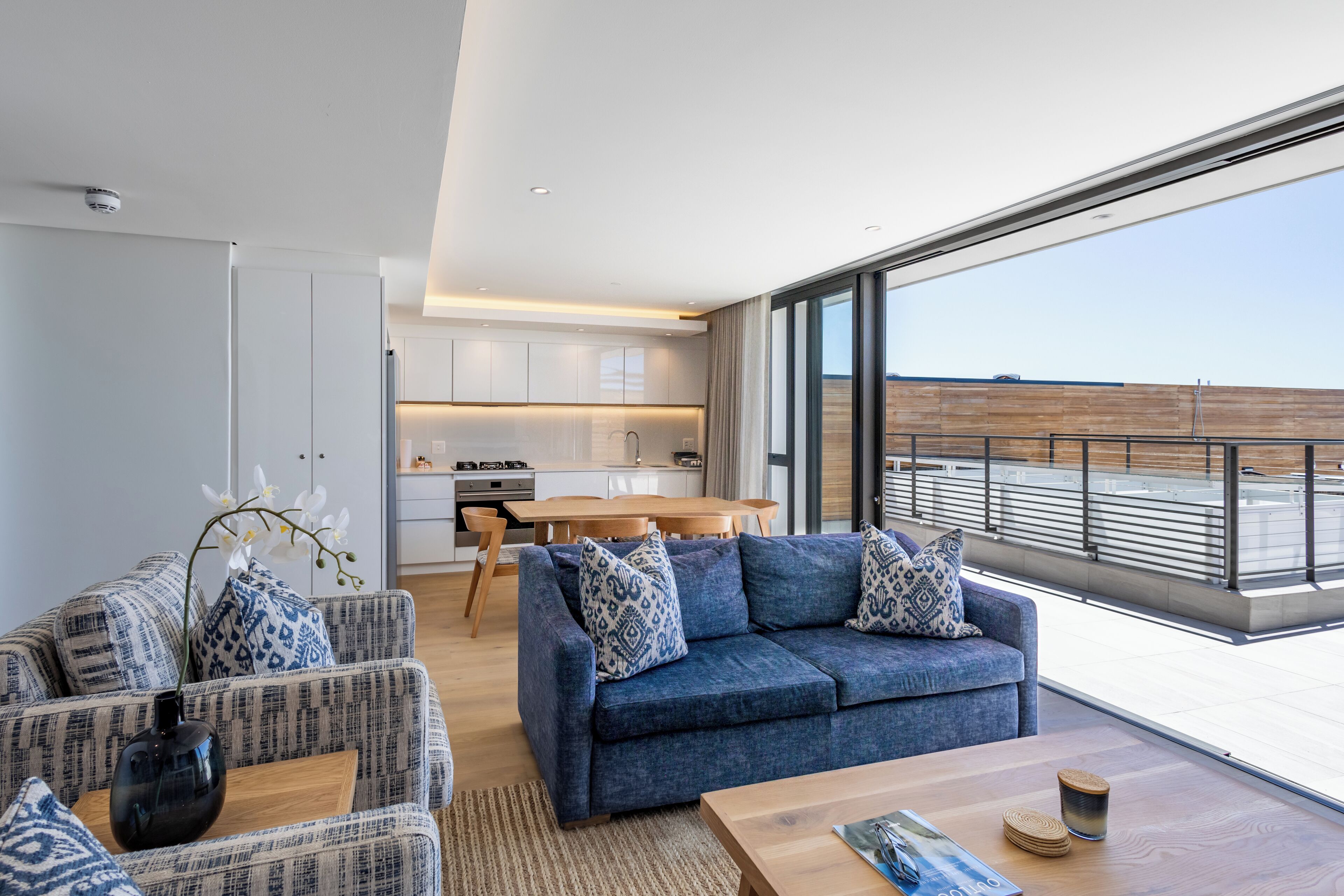 A modern living room with a blue sofa, a wooden coffee table, and a view of the ocean through large windows.