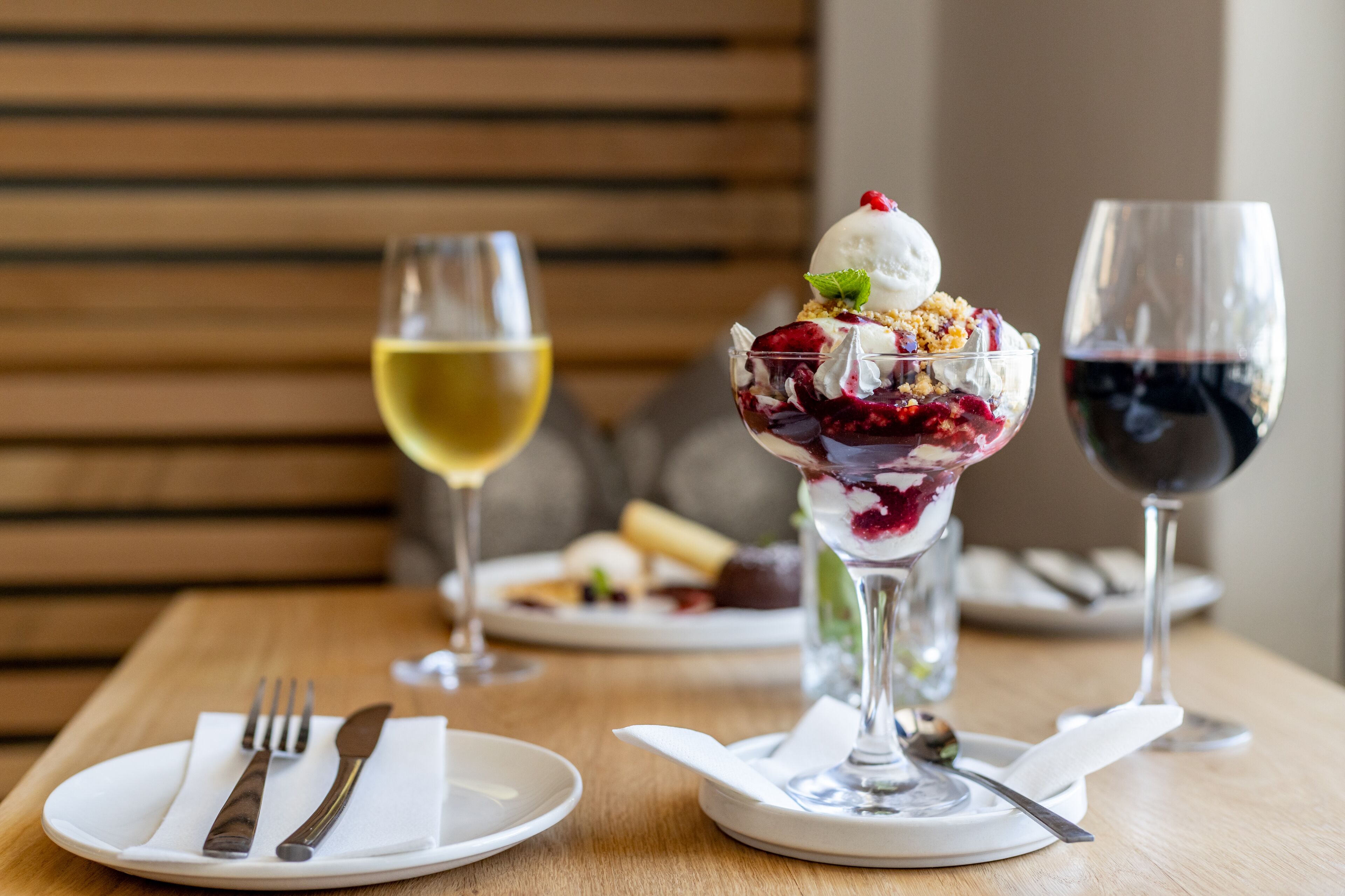 Ein Dessert mit einer Kugel Eis und Beeren auf einem Glas, dazu ein Glas Weißwein und ein Glas Rotwein.