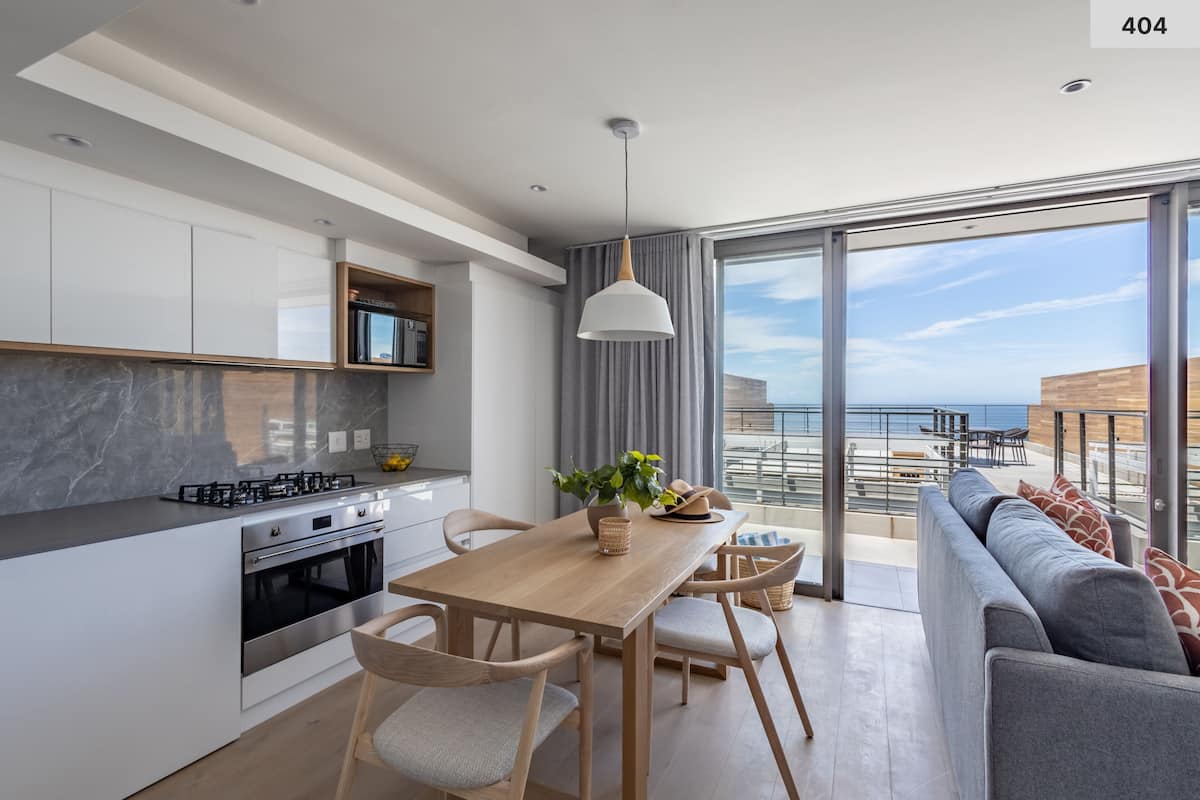 A modern kitchen with a dining area, large windows, and a balcony with a view.