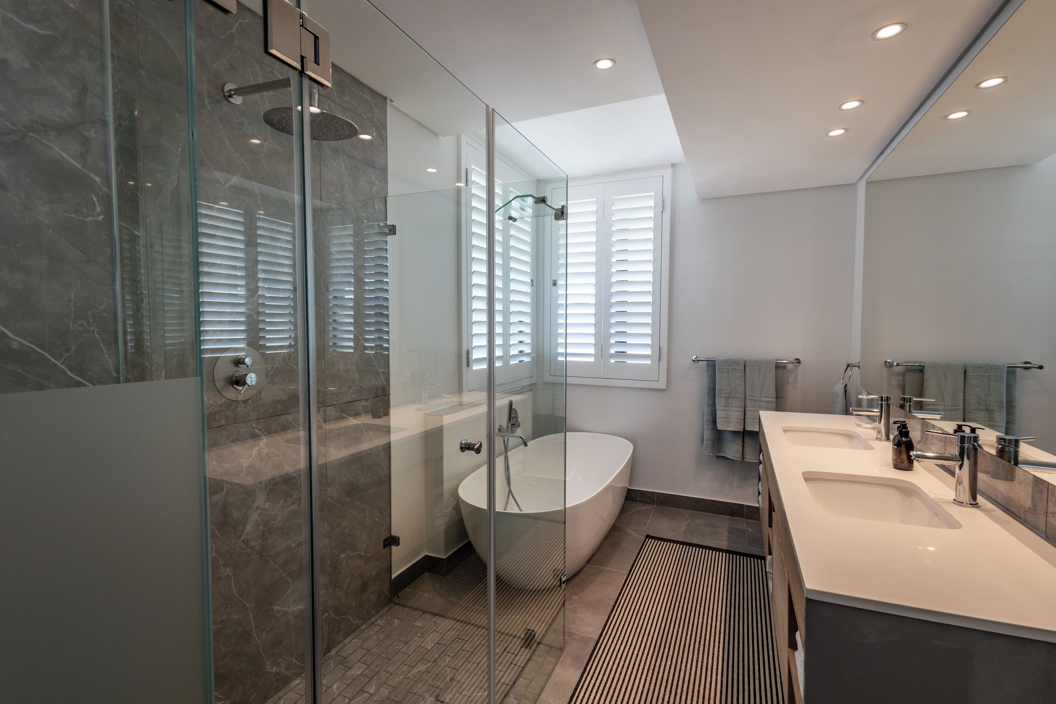 A modern bathroom with a glass-enclosed shower, a freestanding bathtub, and a large vanity with a mirror.
