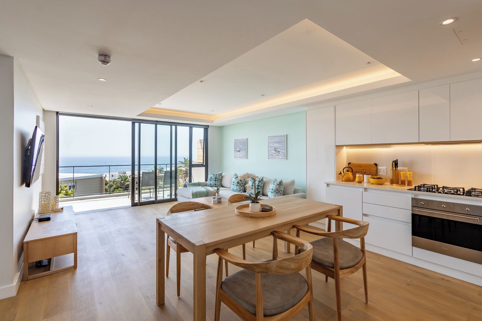 A modern apartment with a dining area, kitchen, and a balcony with a view of the sea.