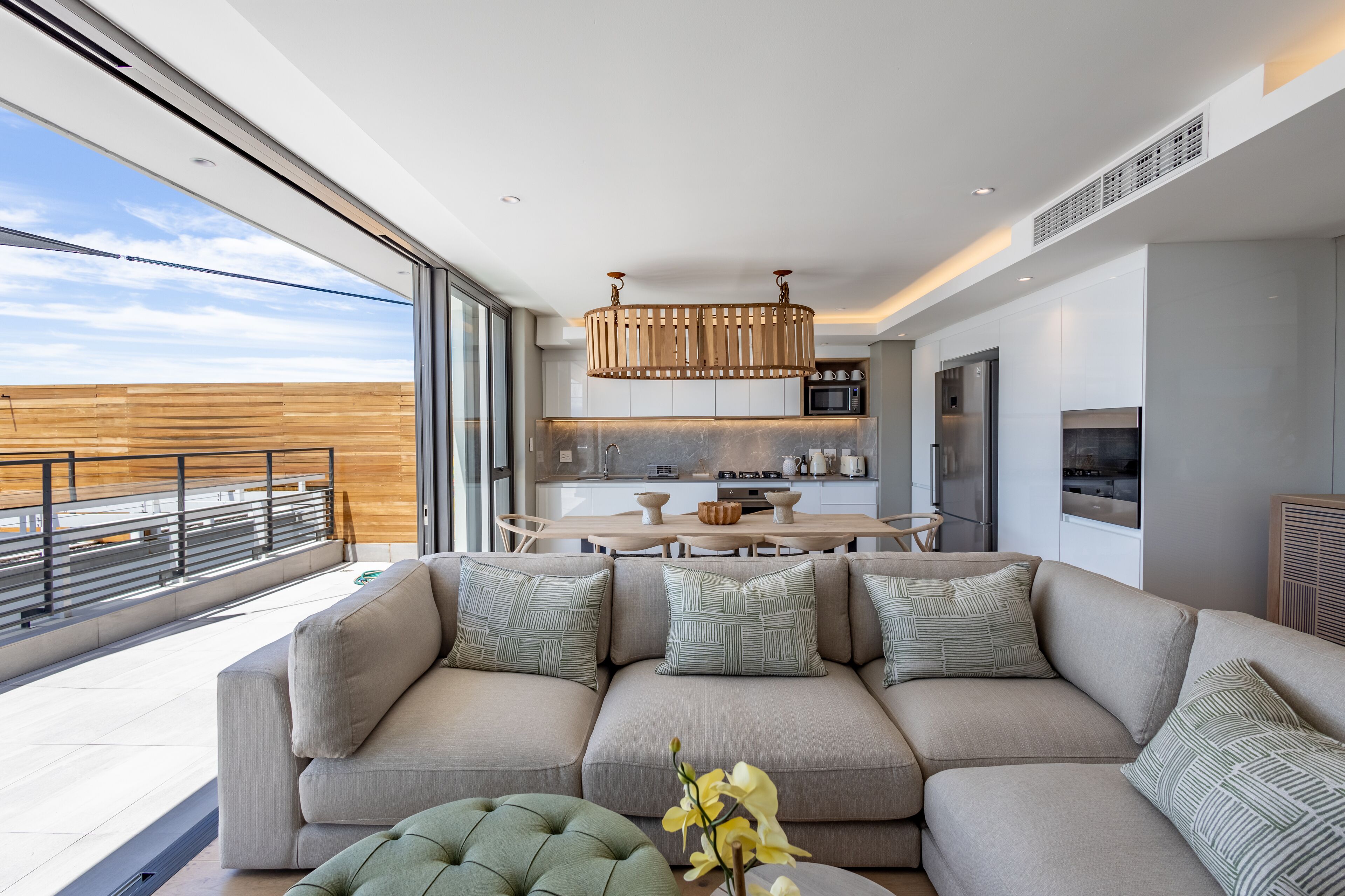 A modern living room with a large sofa, a dining table, and a kitchen in the background.