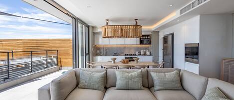 A modern living room with a large sofa, a dining table, and a kitchen in the background.