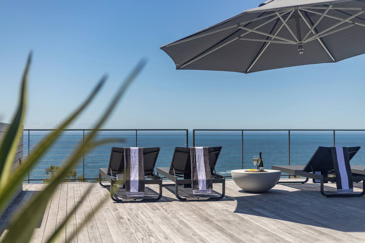 A deck with lounge chairs and a table, overlooking the ocean.