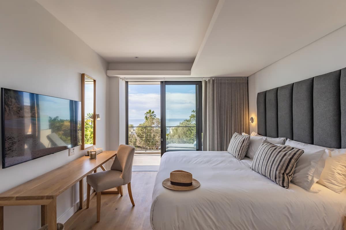 A modern hotel room with a large bed, a desk, and a balcony with a view.