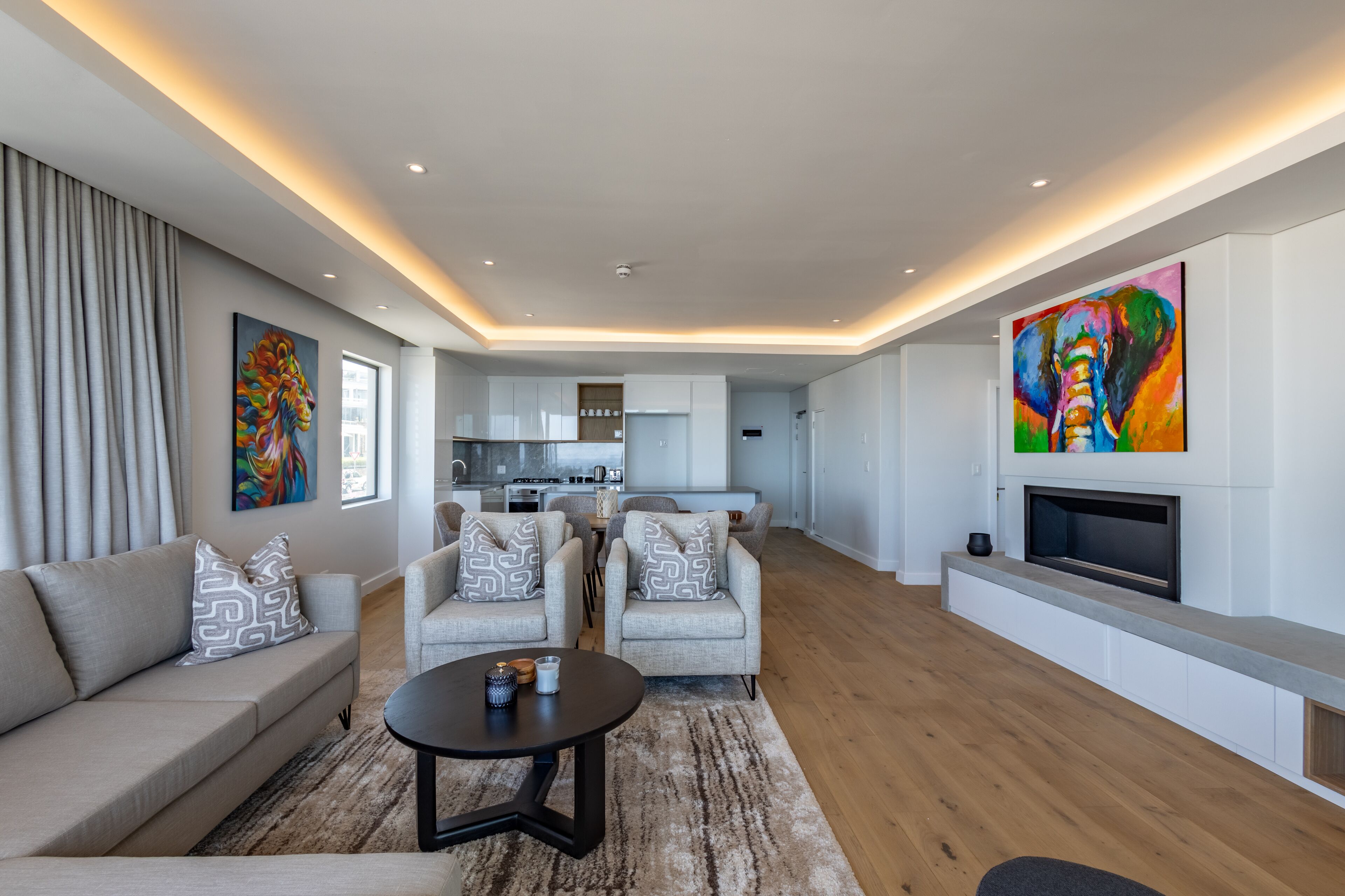 Un salon moderne avec un canapé, des fauteuils, une table basse et un téléviseur fixé au mur.