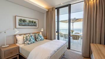 Habitación de hotel con cama, mesita de noche, lámpara y vistas a la terraza con mobiliario exterior.