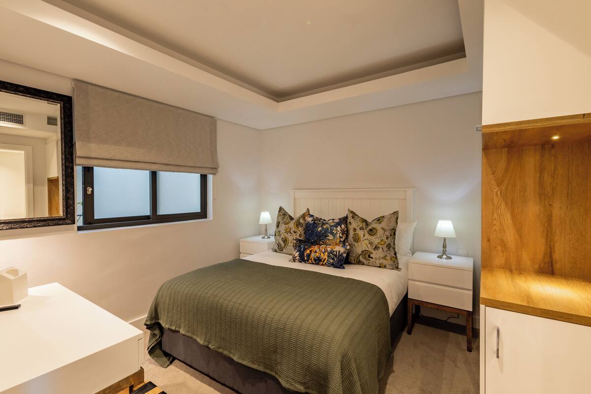 A bedroom with a bed, nightstands, a bedside table, a mirror, and a window with a blind.