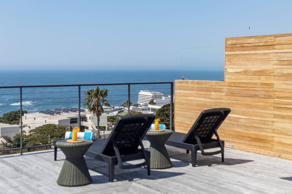 A balcony with two chairs and a small table, overlooking a beach and ocean.