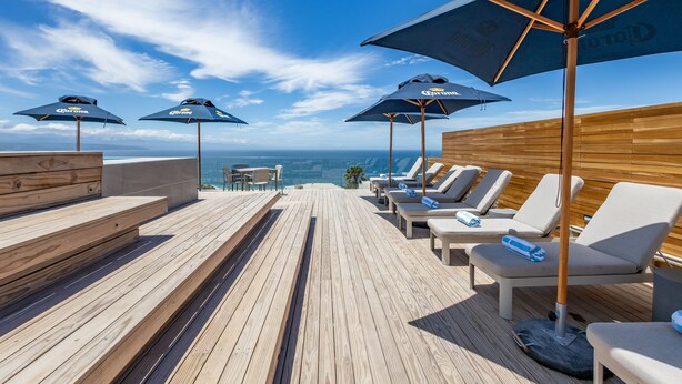 A wooden deck with lounge chairs and umbrellas, overlooking the ocean. - Plett Quarter Apartments (Plettenberg Bay)