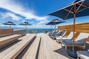 Una terraza de madera con sillones de descanso y sombrillas, con vistas al océano.