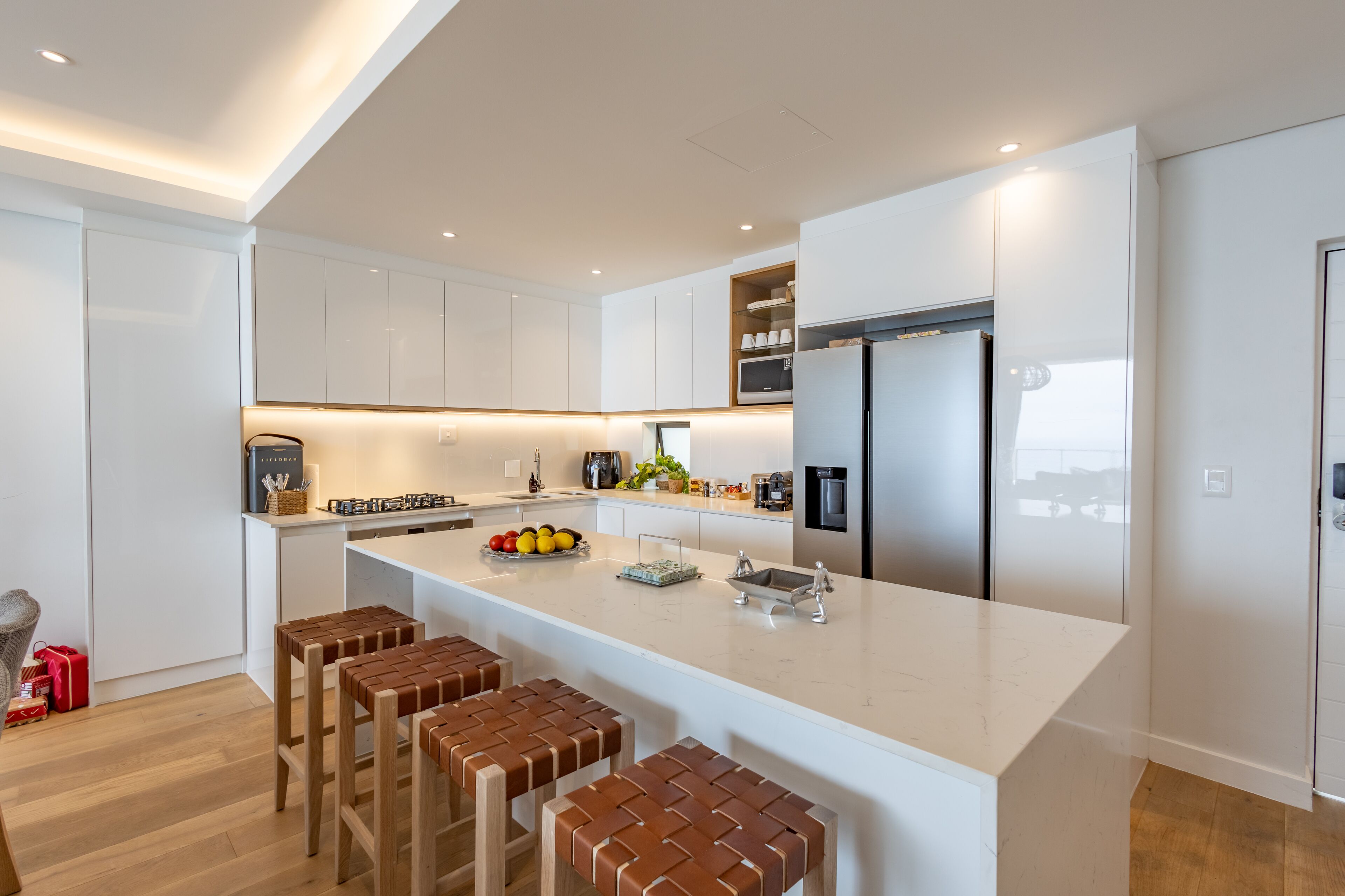 A modern kitchen with white cabinetry, a large island with stools, stainless steel appliances, and a built-in oven.