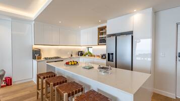 A modern kitchen with white cabinetry, a large island with stools, stainless steel appliances, and a built-in oven.