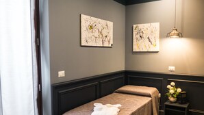 A spa room with two beds, a small table with a vase of flowers, and two abstract paintings on the wall. - Host'n GO (Colleferro)