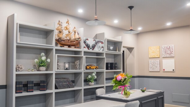 A modern kitchen with white cabinetry, a dining table with two chairs, and a decorative ship model on the shelves. - Host'n GO (Colleferro)