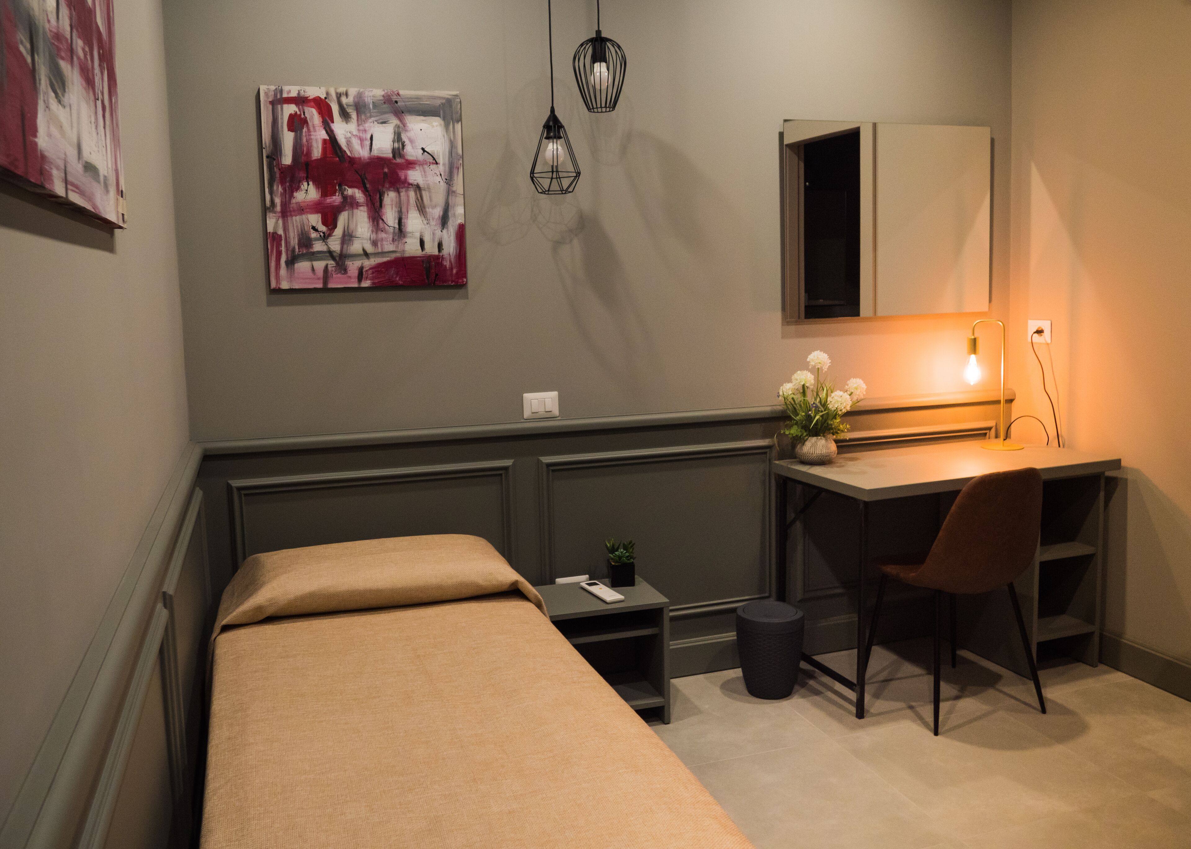 Een kleine, moderne kamer met een bed, een bureau, een stoel, een kleine plant en een spiegel aan de muur.