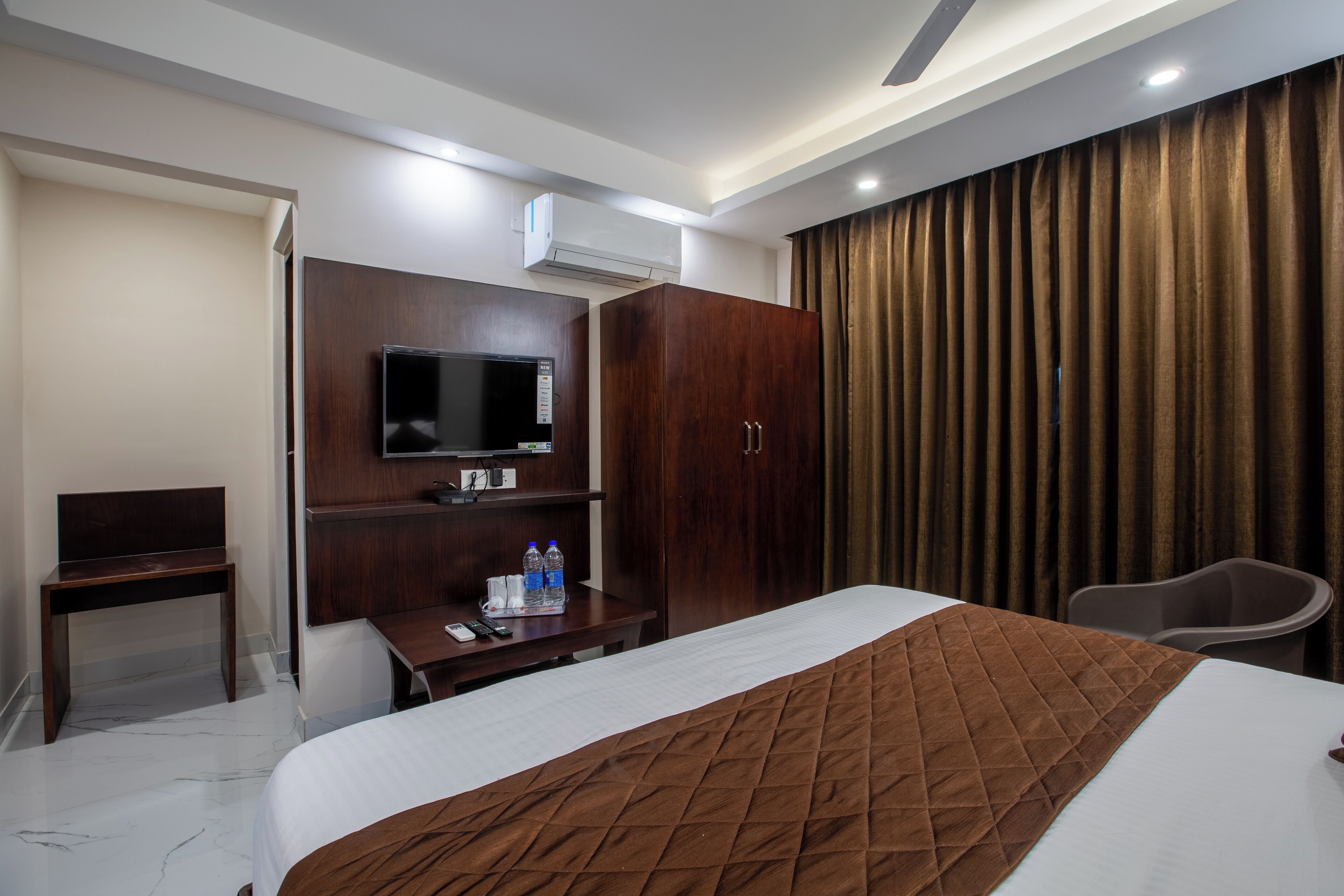 A hotel room with a bed, a desk, a chair, a television, and a wardrobe.