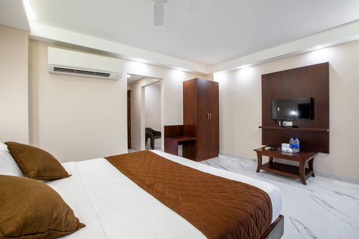 A hotel room with a bed, a wardrobe, a TV, and a small table with a remote control and water bottles.