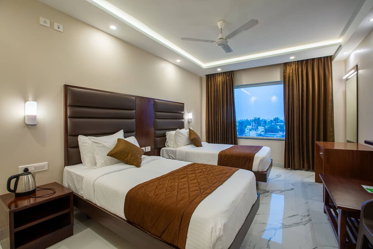 A hotel room with two beds, a desk, a chair, a nightstand, a kettle, and a large window with curtains.