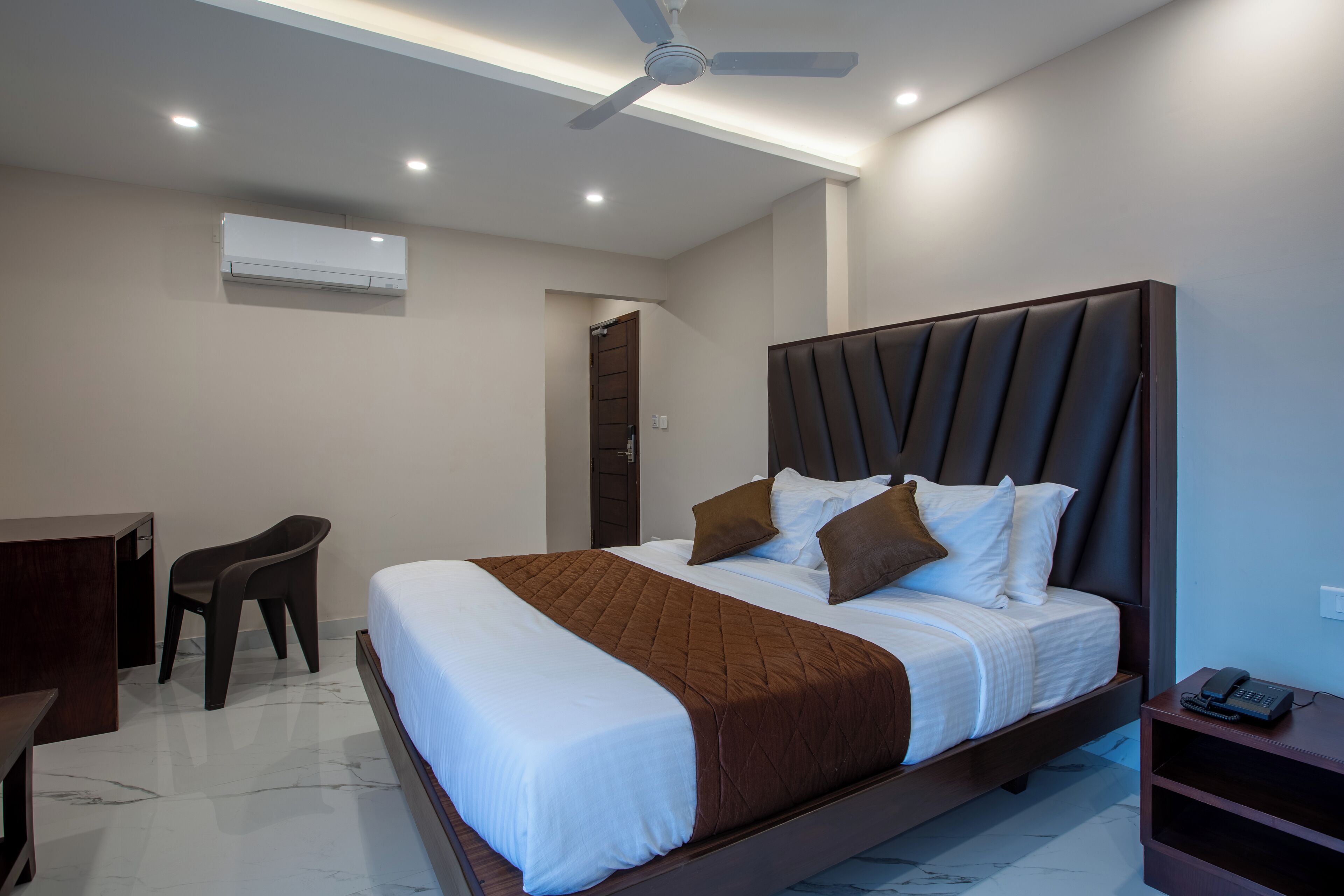 Una habitación de hotel moderna con una cama grande, un escritorio, una silla y un ventilador de techo.