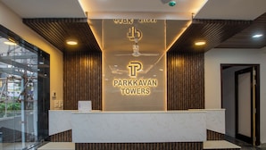 A reception area with a modern design, featuring a reception desk, a ceiling fan, and a sign for Parkkavan Towers. - PARKKAVAN TOWERS (Manachanallur)